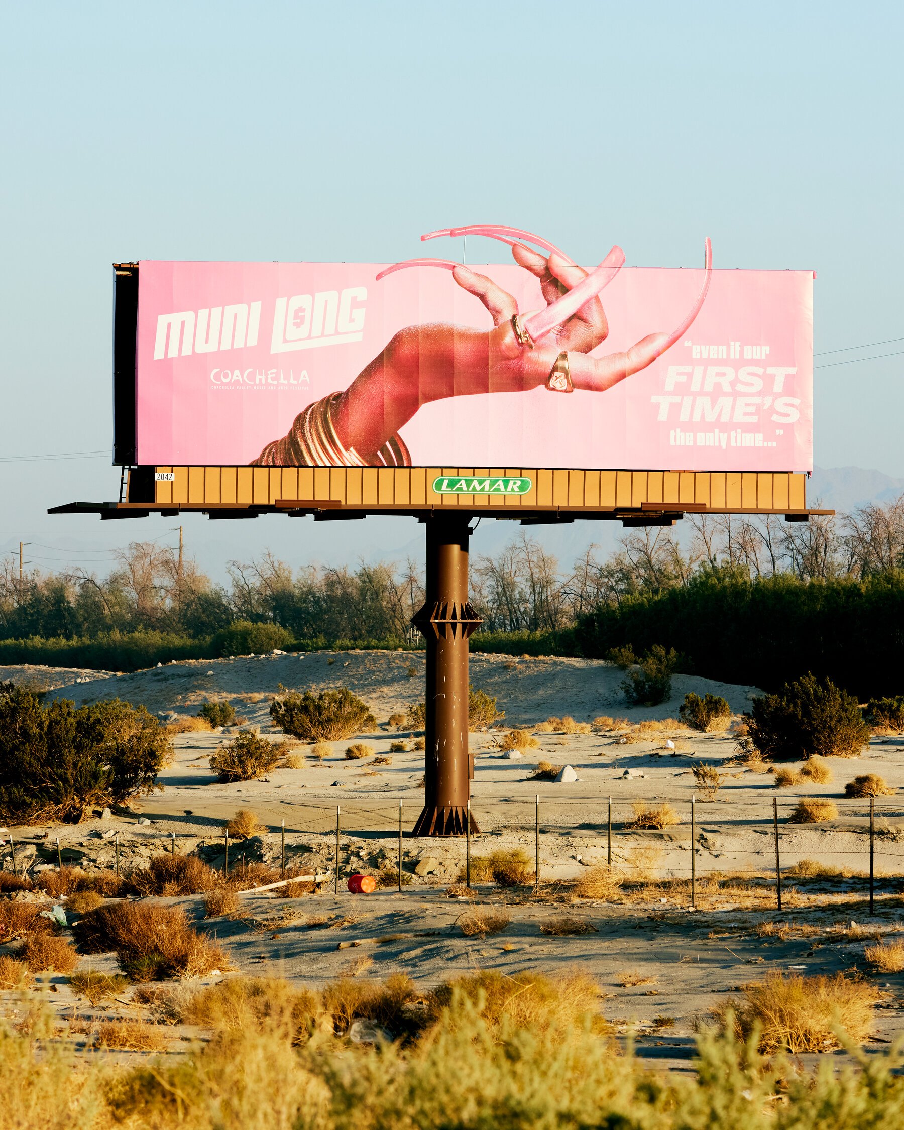 A pink Coachella billboard rises out of the desert. Minimal words, maximum signal.