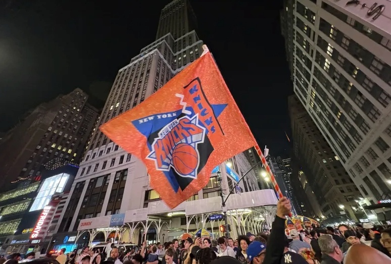 Fan waving a New York Knicks flag in front of Madison Square Garden as crowds celebrate the Finals run